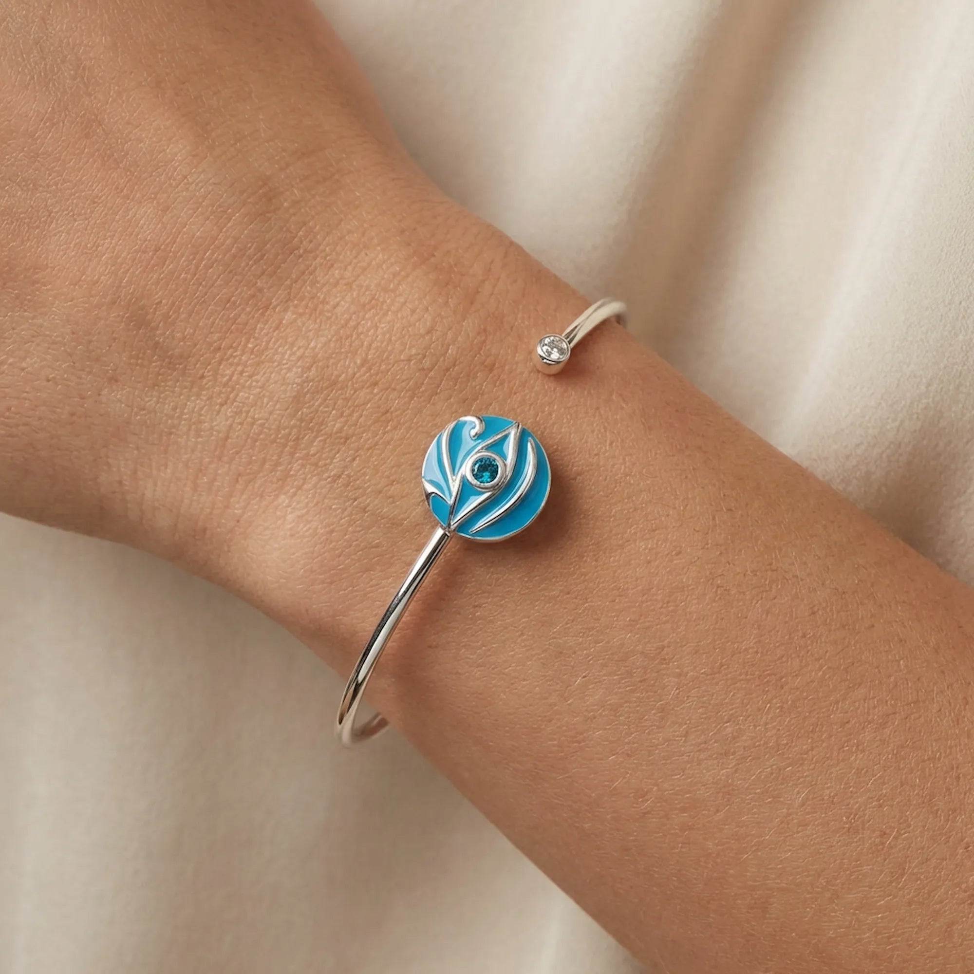 Close-up of azure blue topaz evil eye cuff bangle on wrist, white fabric background, Luna Dura