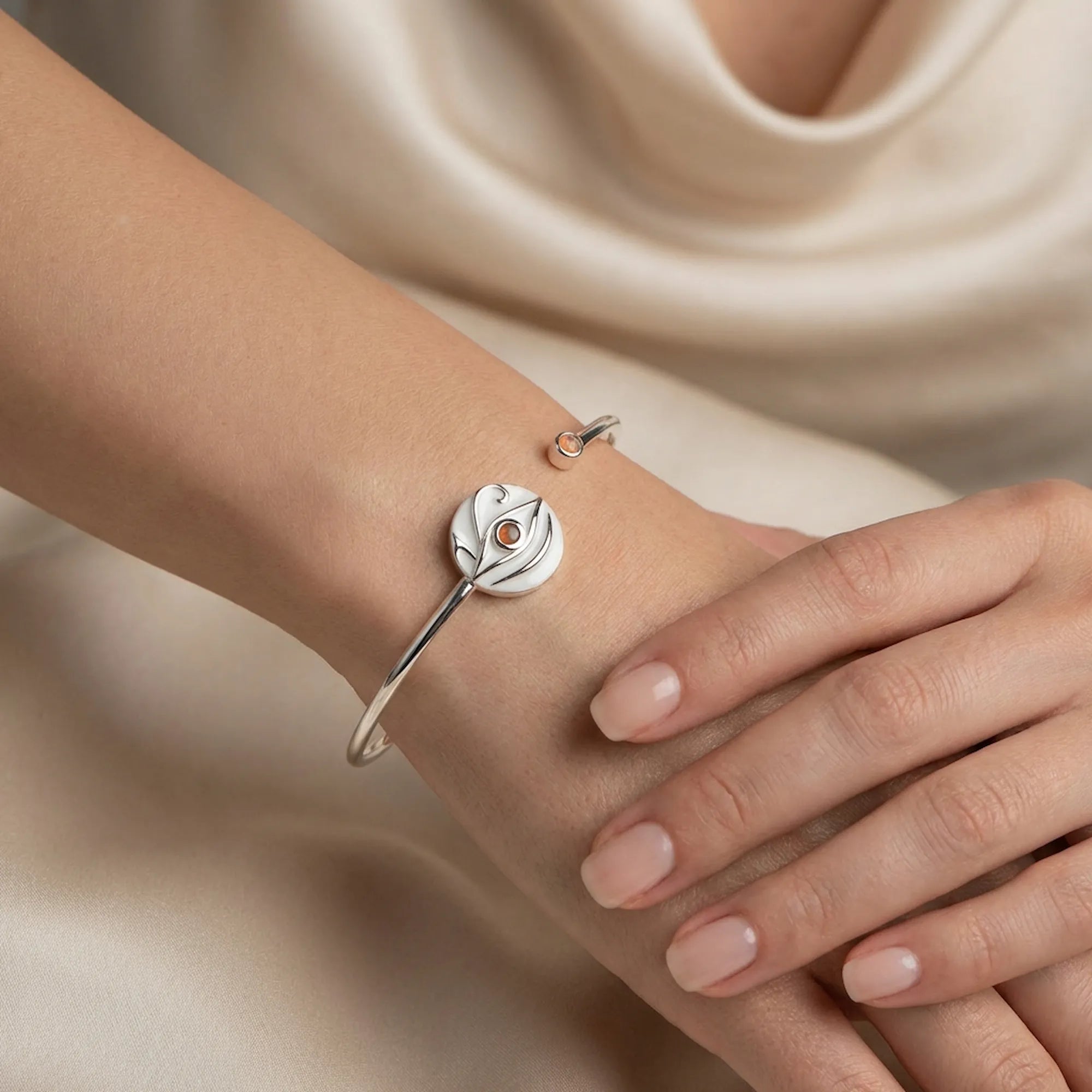 Close-up of white dual opal evil eye cuff bangle worn on wrist, cream satin fabric background
