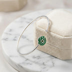 Green peridot evil eye cuff bangle resting on cream jewellery box on white marble
