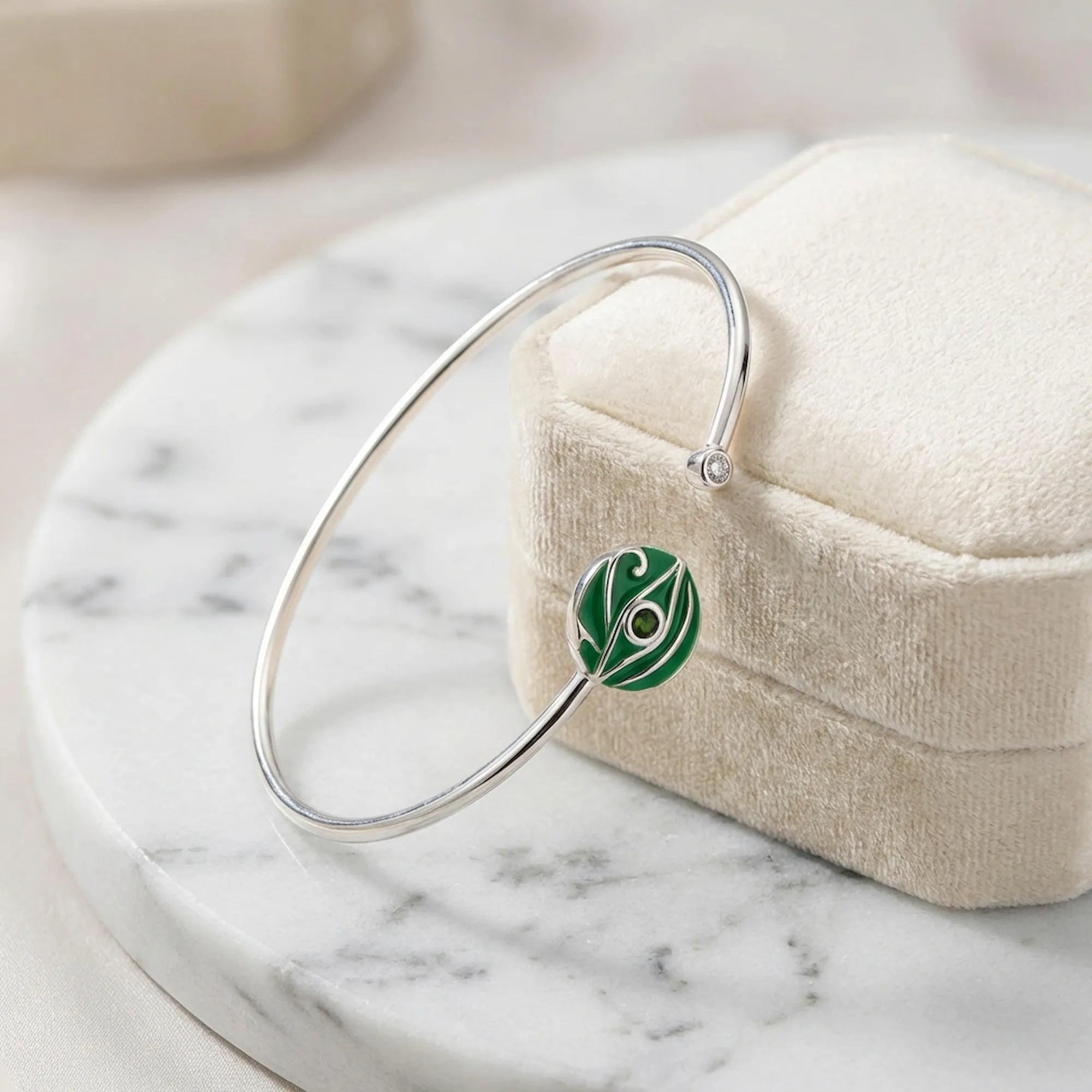 Green peridot evil eye cuff bangle resting on cream jewellery box on white marble