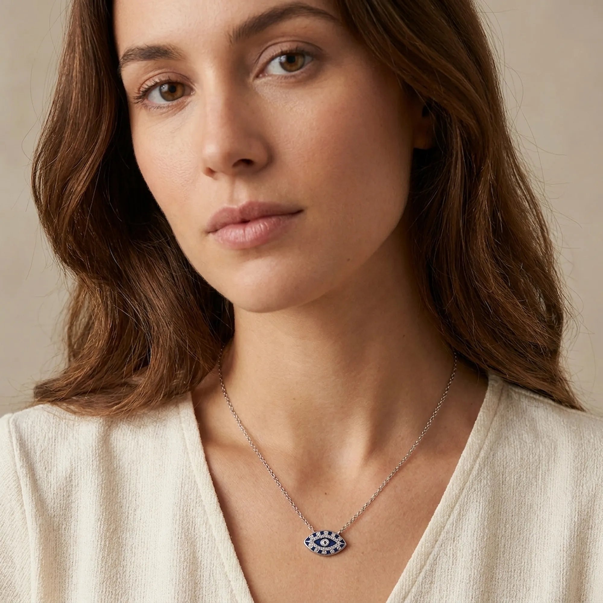 Royal blue enamel evil eye pendant necklace worn at upper chest on 925 silver cable chain, warm neutral background