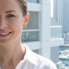 Smiling woman wearing extra-large CZ silver hoops by the water at Dubai Marina.