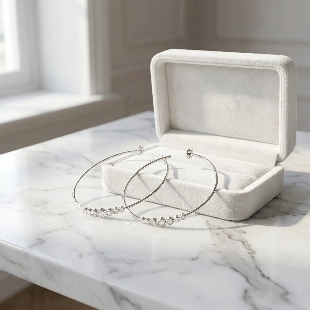 Large CZ silver hoop earrings beside a cream velvet gift box on marble. Luna Dura Dubai.