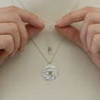 Hands holding Eye of Horus white enamel necklace showing spring ring clasp and adjustable chain detail