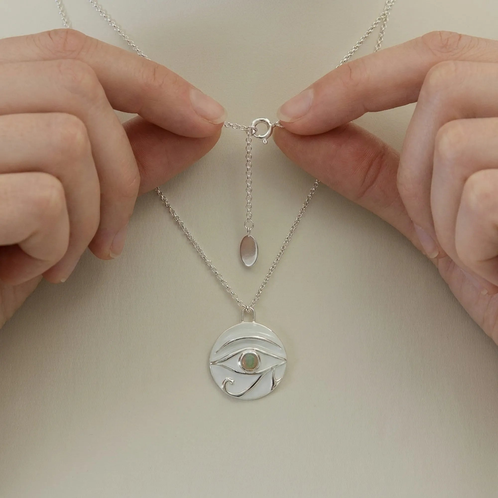 Hands holding Eye of Horus white enamel necklace showing spring ring clasp and adjustable chain detail