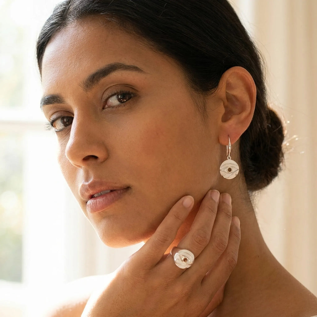 Woman wearing Eye of Horus white enamel earring and signet ring with yellow fire opal, studio, Luna Dura