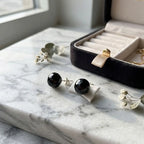 Faceted black resin stud earrings with 925 sterling silver posts displayed on white marble beside an open jewellery box.