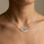 Close view of a sterling silver feather necklace with turquoise crystal at the collarbone, Luna Dura Dubai.