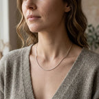 Woman wearing a delicate silver-tone bar-link chain necklace with a soft grey V-neck knit top.