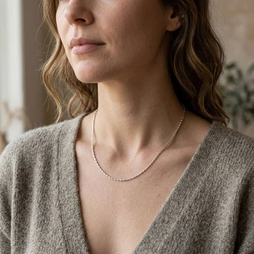 Woman wearing a delicate silver-tone bar-link chain necklace with a soft grey V-neck knit top.