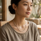 Woman wearing a fine bright silver-tone necklace with a beige blouse.