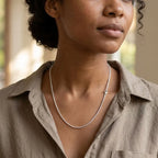 Woman wearing a fine silver-tone textured chain necklace with a taupe collared shirt.
