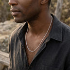 Man wearing a fine silver-tone twisted-link necklace with an open-collar charcoal shirt.