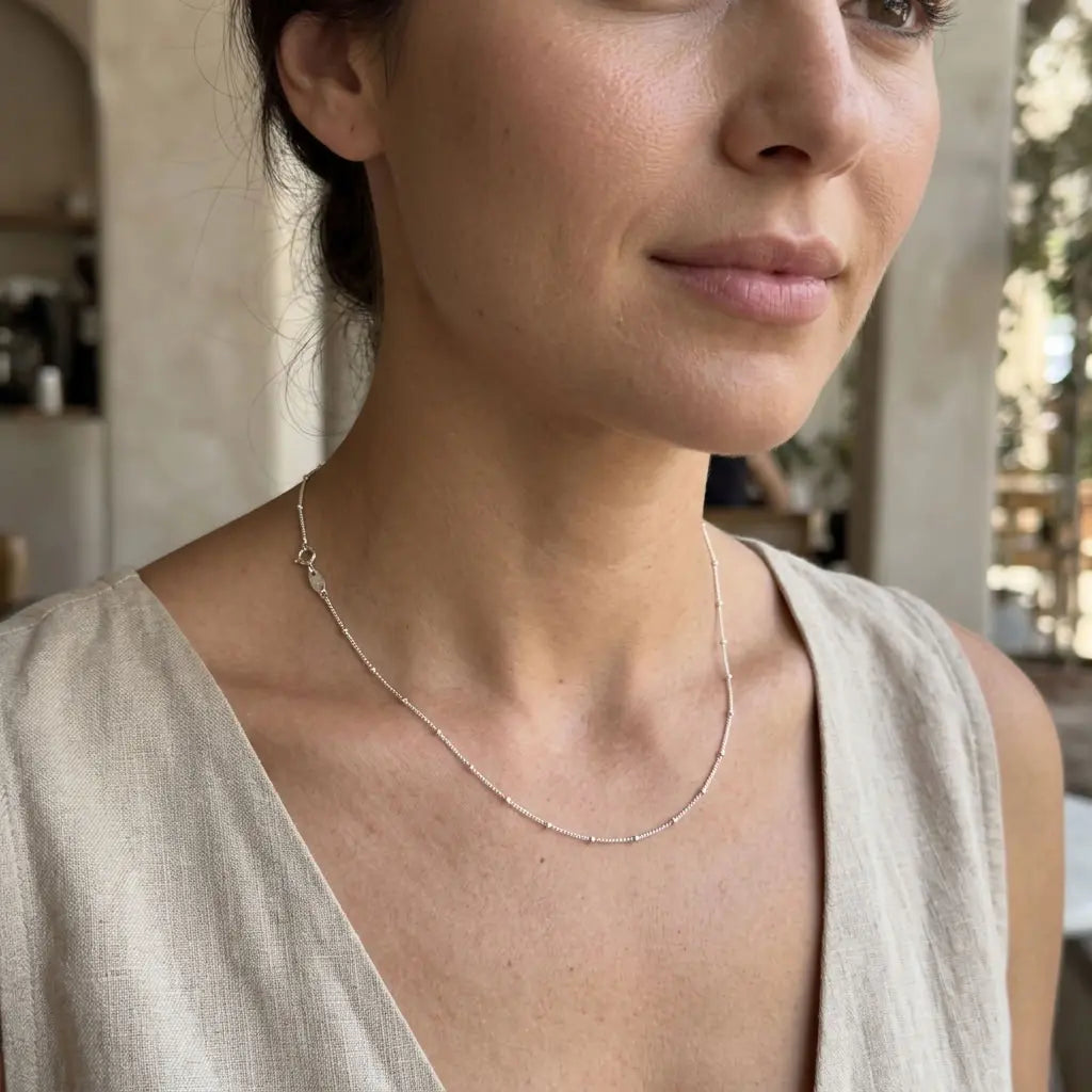 Woman wearing a delicate silver satellite station necklace with a cream sleeveless top.