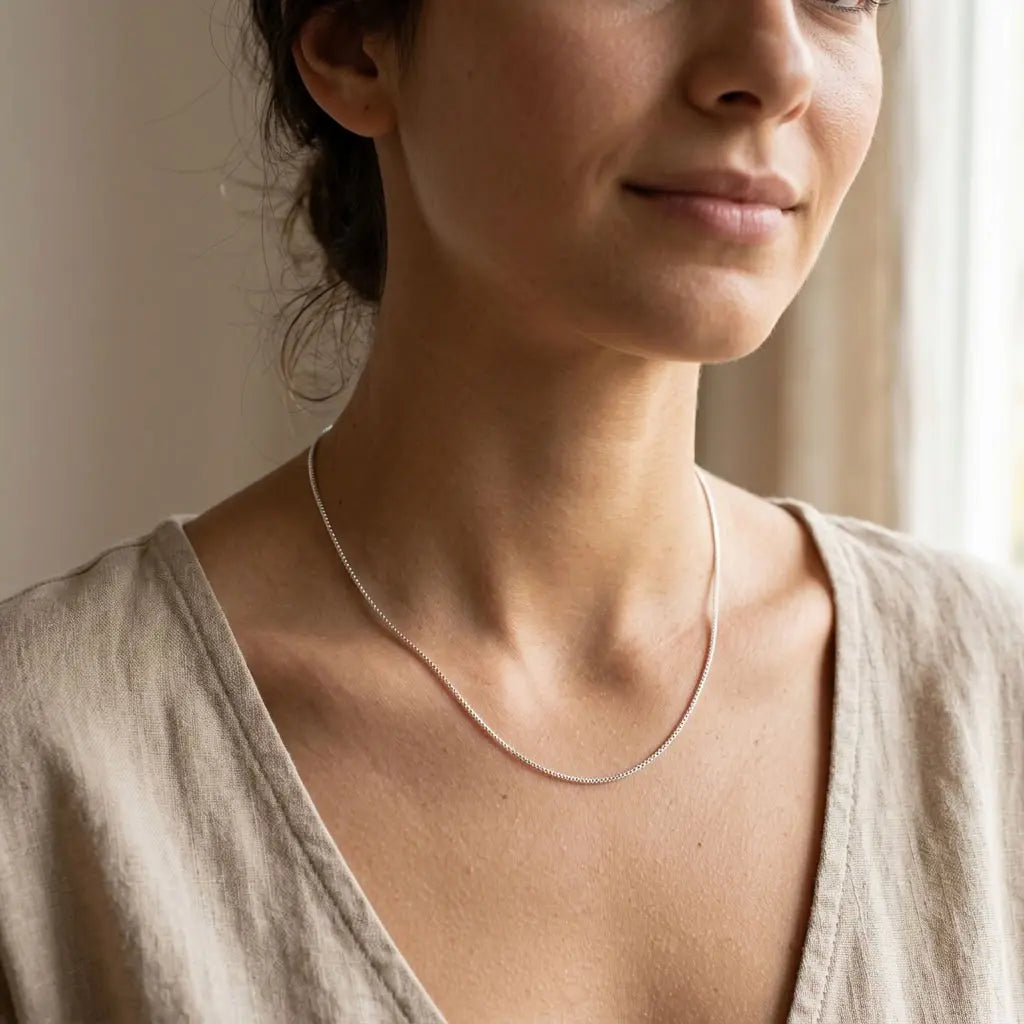Woman wearing a fine silver box chain necklace with a cream V-neck blouse.