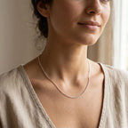 Woman wearing a fine silver box chain necklace with a cream V-neck blouse.