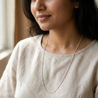 Woman wearing a long, fine silver curb-style chain necklace with a beige blouse.