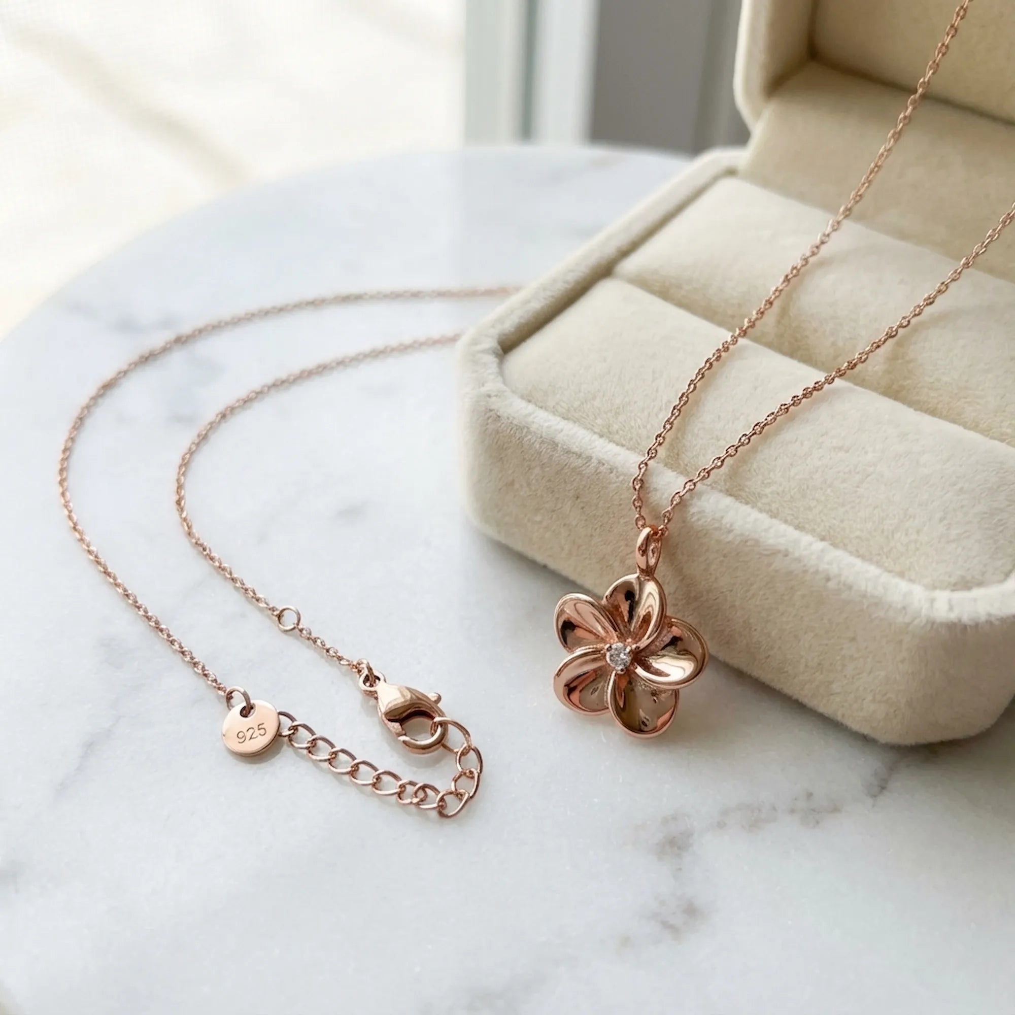Rose gold pendant necklace clasp detail showing 925 stamp tag and extender chain on marble surface