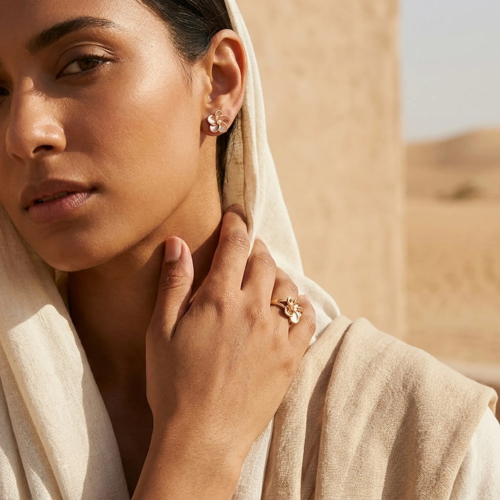 Model wearing rose gold floral stud earrings and matching ring against desert landscape, Dubai