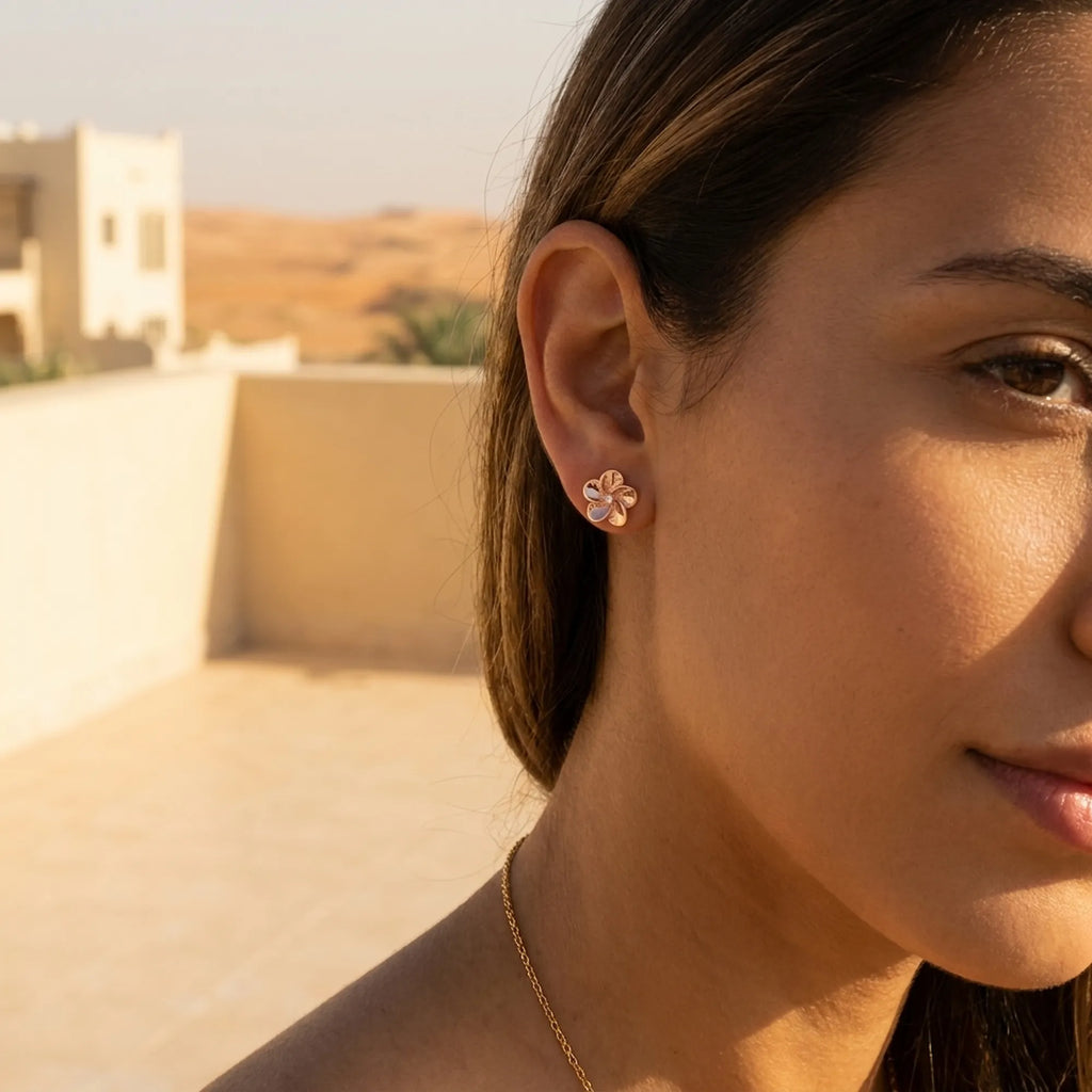 Rose gold flower stud earring worn on ear with desert architecture in background, Dubai lifestyle shot