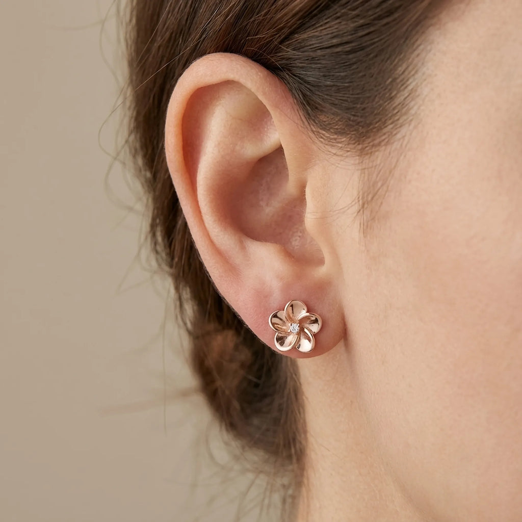 Floral rose gold stud earring on ear against neutral beige background — 10 mm polished petals, CZ centre