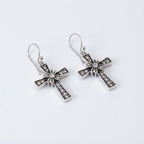 Floriated cross dangle earrings in oxidised 925 sterling silver, angled view — rhinestone pavé and floral starburst centre