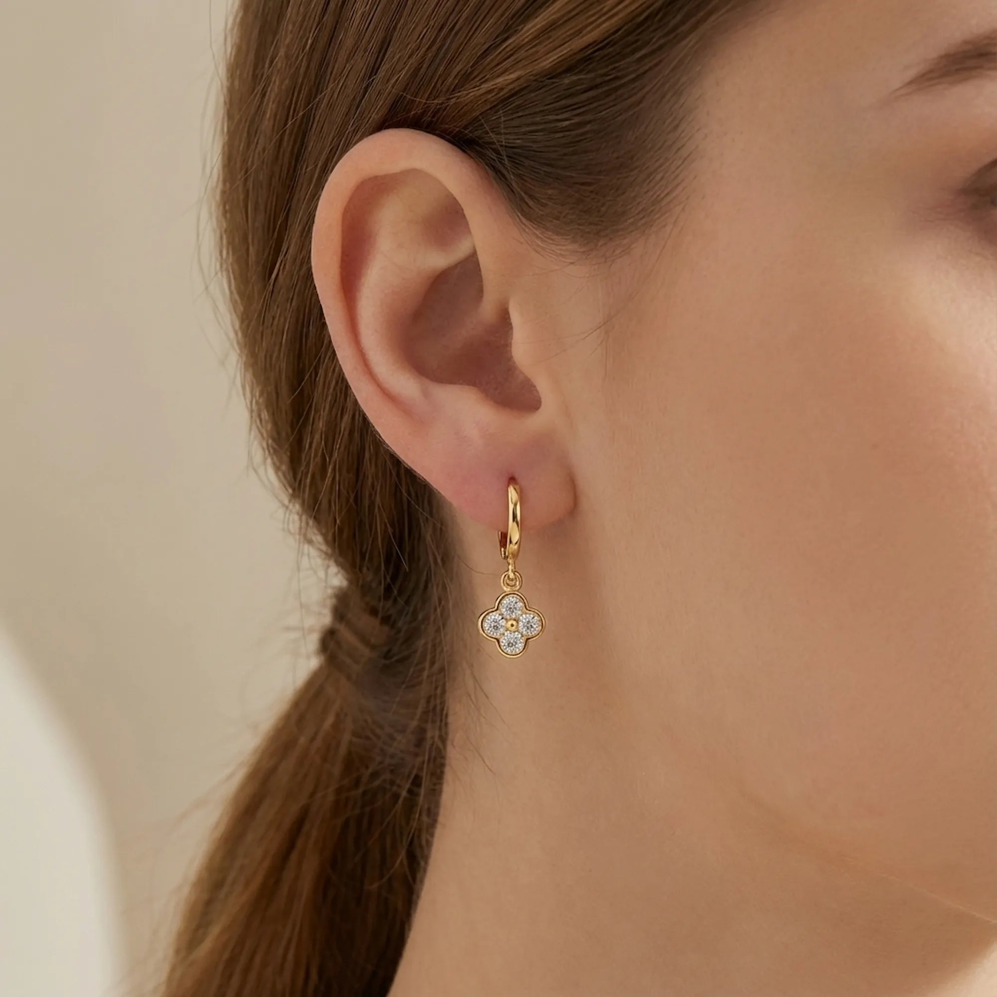 Woman wearing a gold four-leaf clover huggie hoop earring, Luna Dura Dubai.