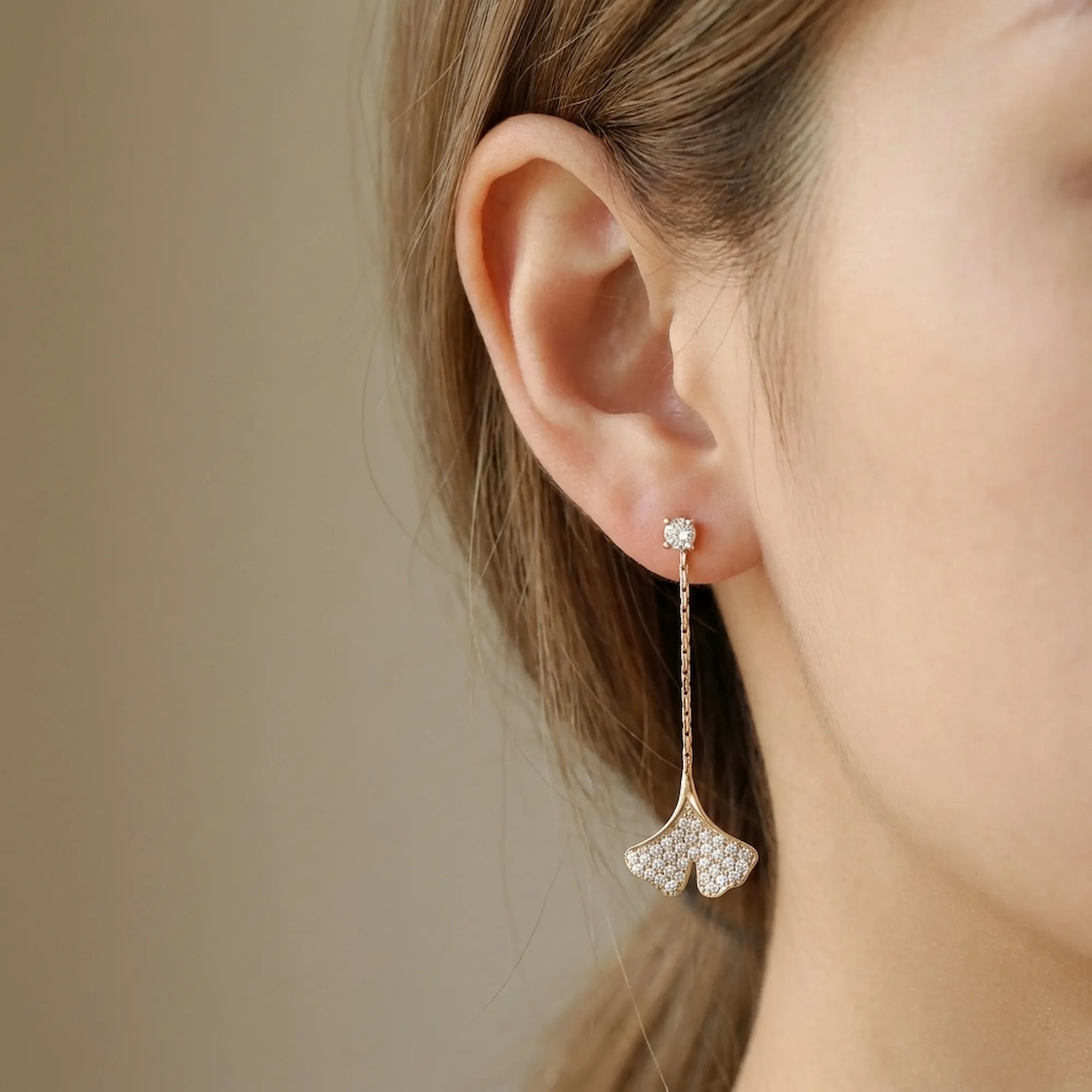 Close-up of ginkgo leaf drop earring in 18K gold with pave CZ on model ear, warm skin tone