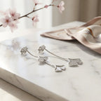 Rhodium silver ginkgo drop earrings on white marble with cherry blossom branch, styled flat lay