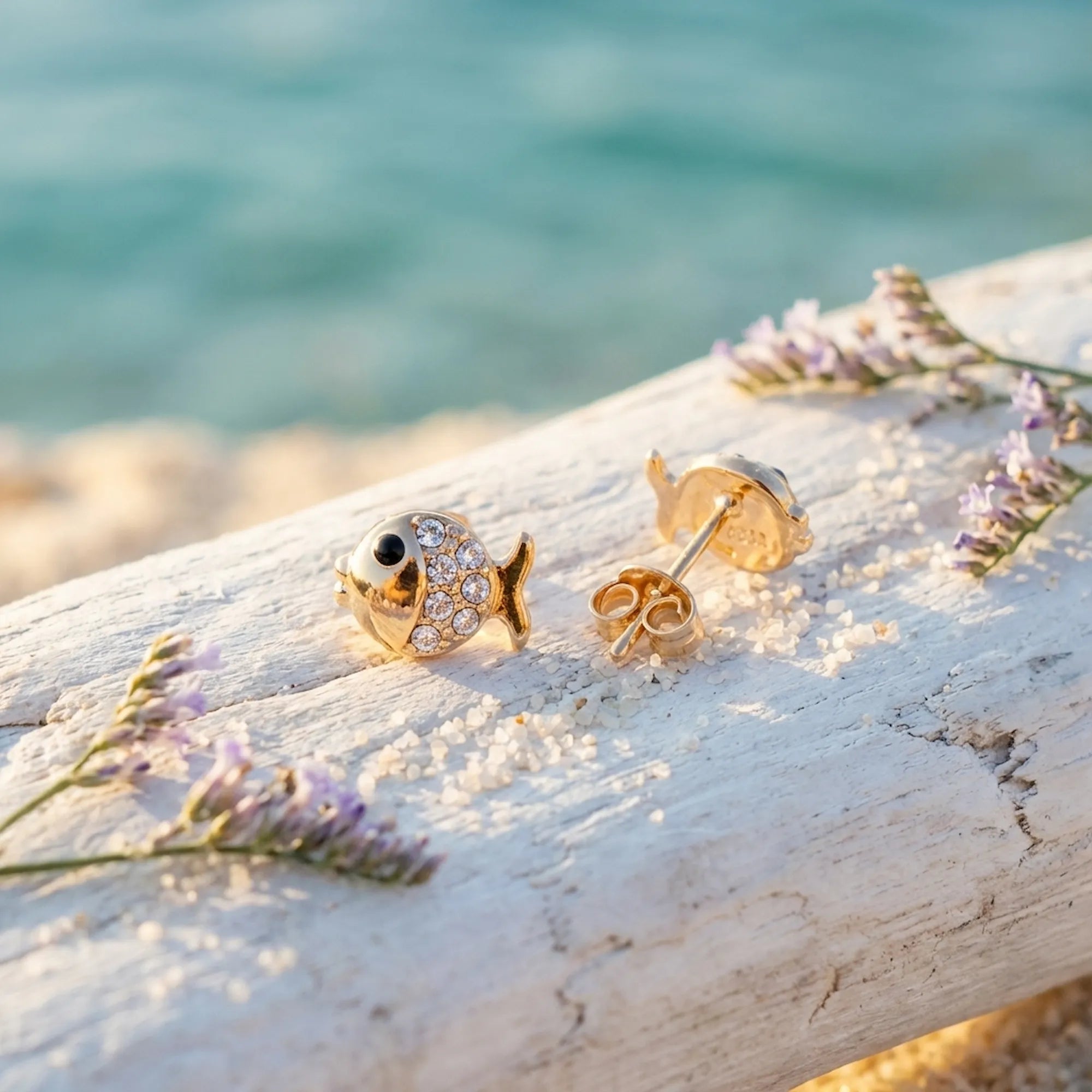 Goldfish stud earrings on driftwood at beach — 18K gold 925 silver, turquoise sea background, lavender flowers