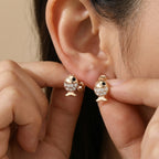 Close-up of goldfish stud earring being placed on ear — CZ scales and black eye detail, neutral background