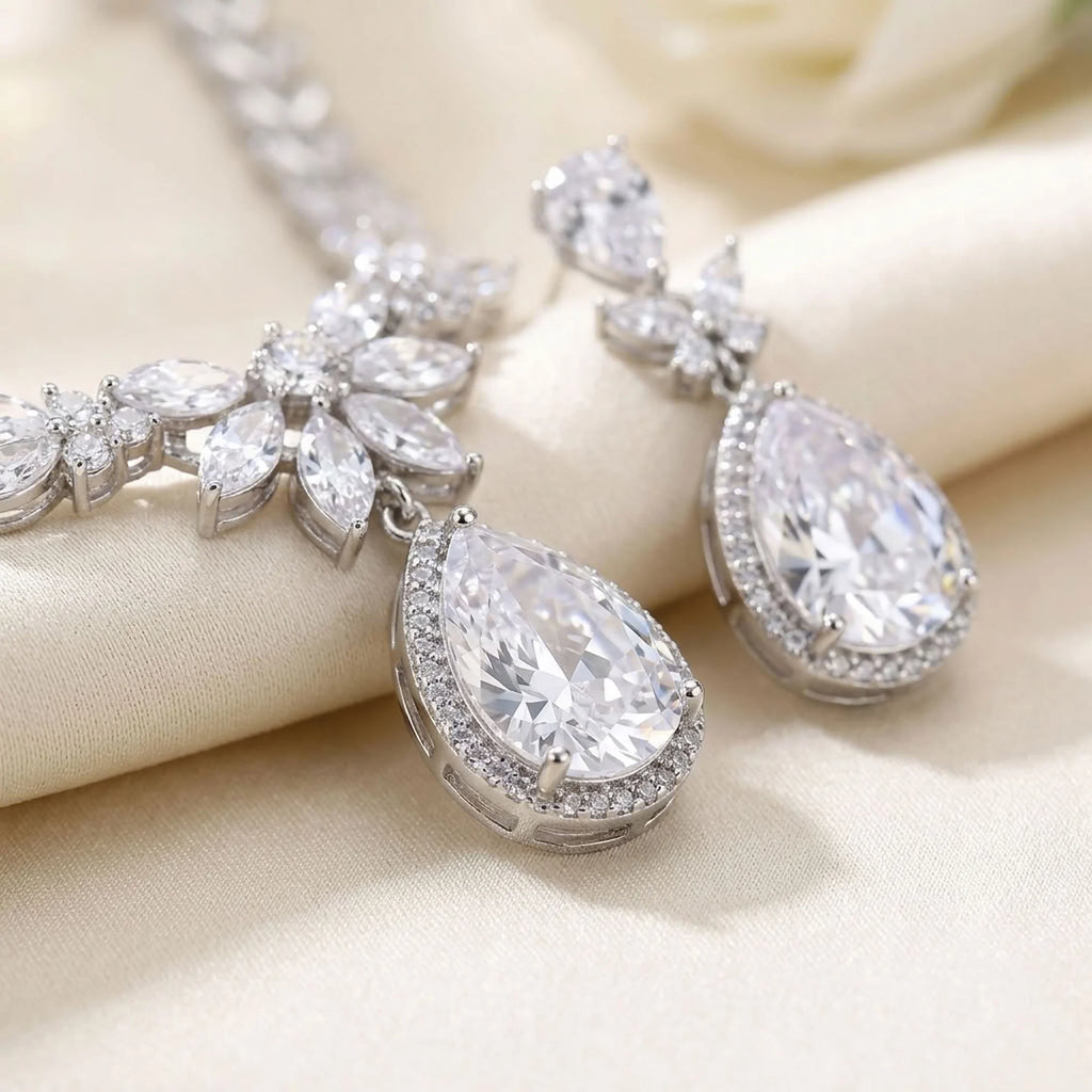 Close-up of rhodium-plated cubic zirconia halo teardrop earrings and marquise necklace resting on silk in Dubai.