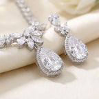 Close-up of rhodium-plated cubic zirconia halo teardrop earrings and marquise necklace resting on silk in Dubai.