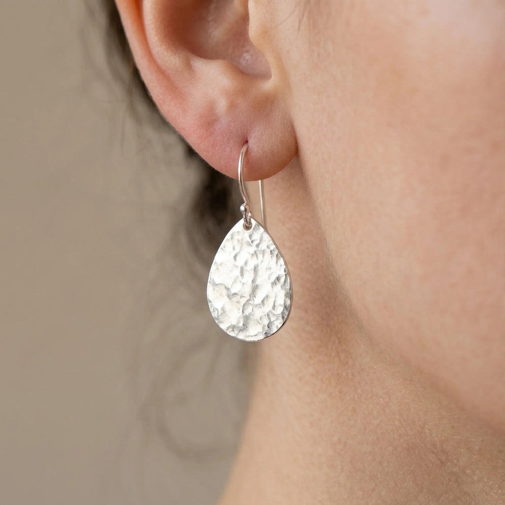 Woman wearing hammered teardrop 925 sterling silver everyday drop earrings indoors in Dubai.