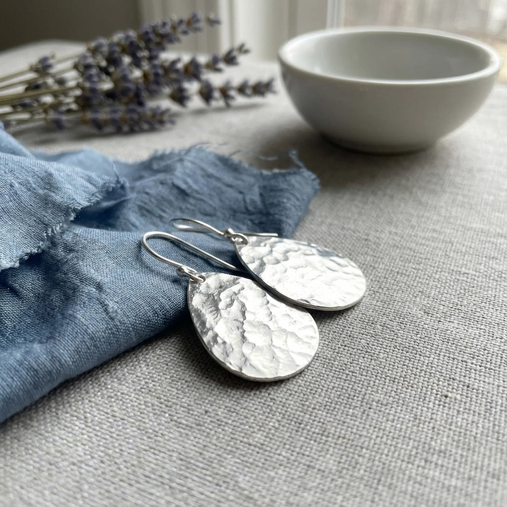 Hammered teardrop 925 sterling silver earrings flat on blue fabric, an everyday jewelry piece in Dubai.