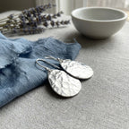 Hammered teardrop 925 sterling silver earrings flat on blue fabric, an everyday jewelry piece in Dubai.