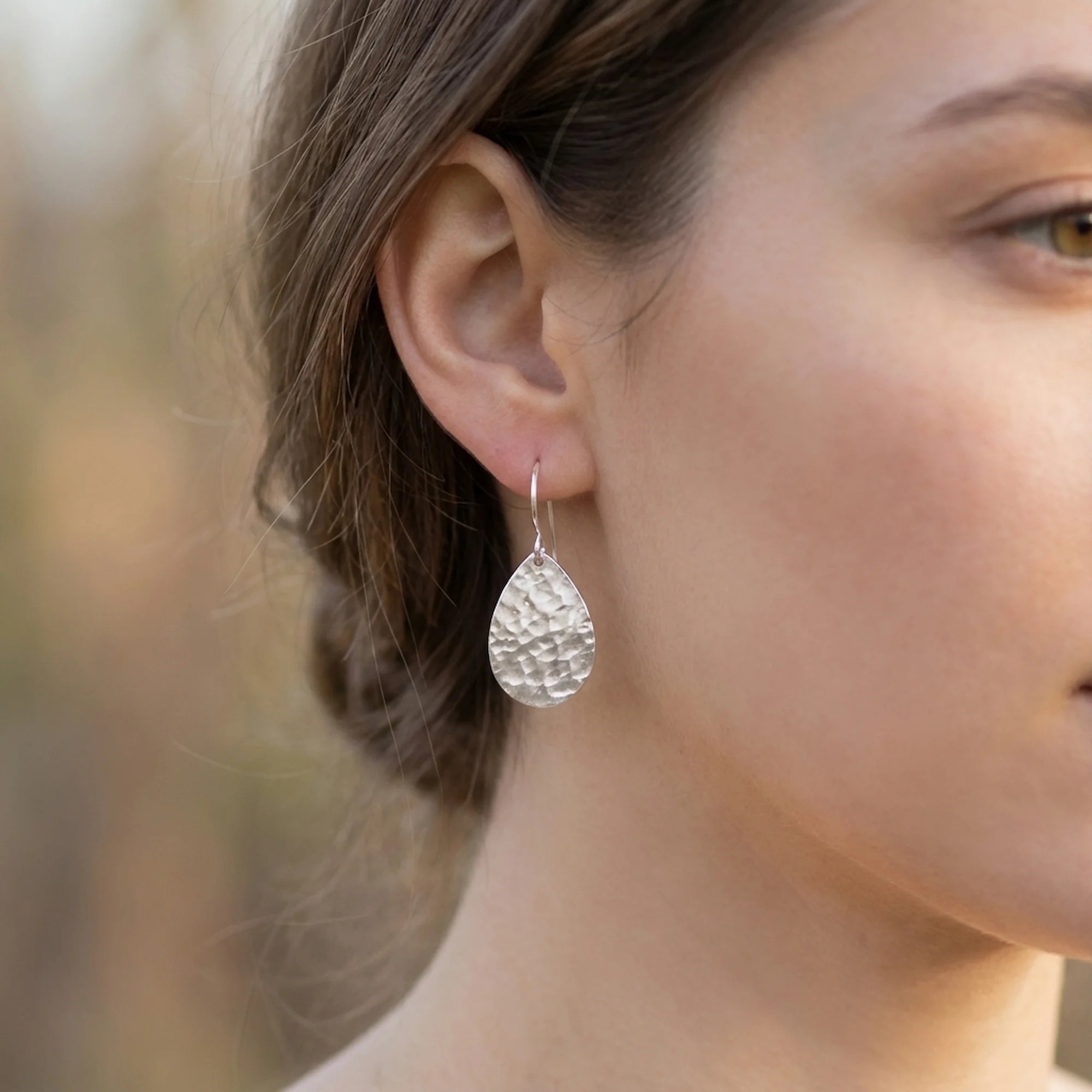 Woman outdoors in Dubai wearing hammered teardrop 925 sterling silver drop earrings with shepherd hooks.