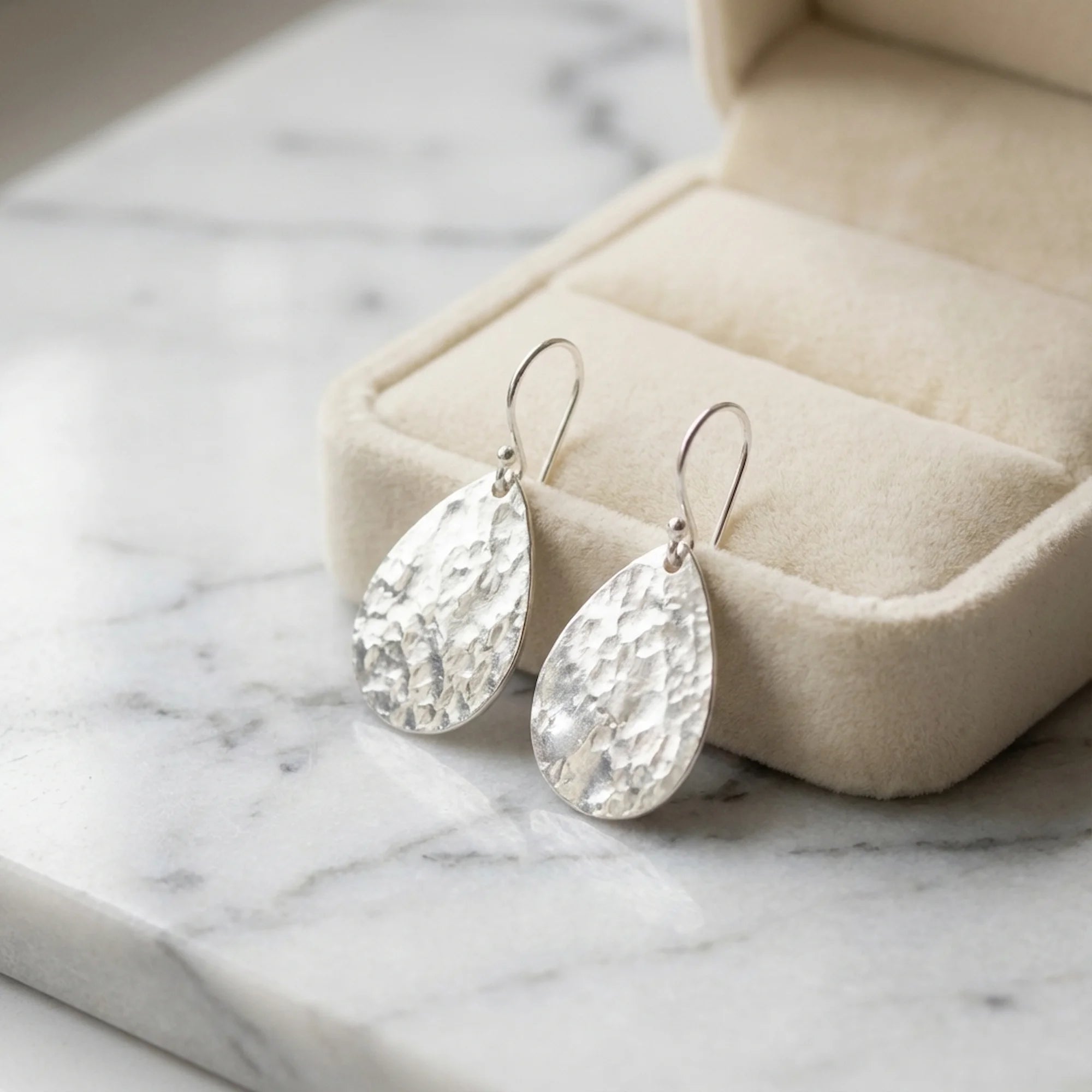 Hammered teardrop 925 sterling silver drop earrings with shepherd hooks resting in a box in Dubai.