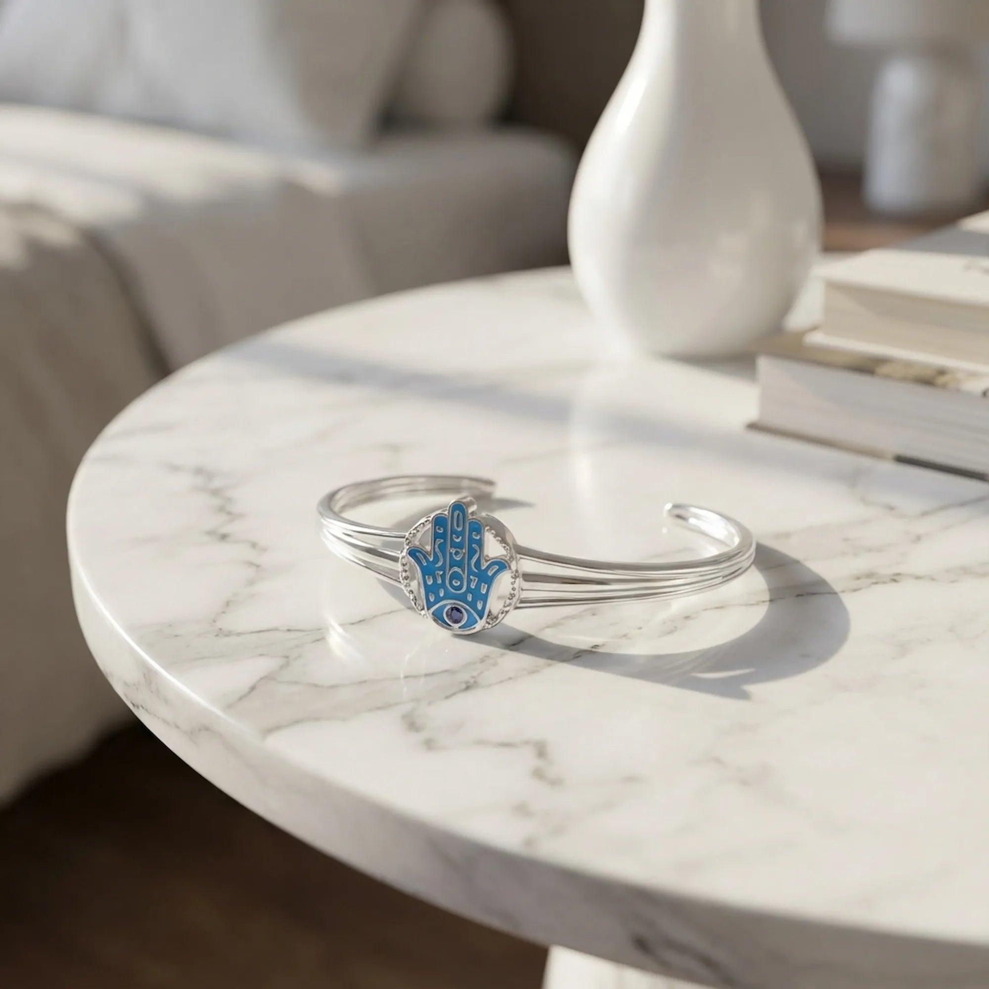 Azure blue enamel Hamsa silver bangle on marble surface, tanzanite eye and carved motif detail visible