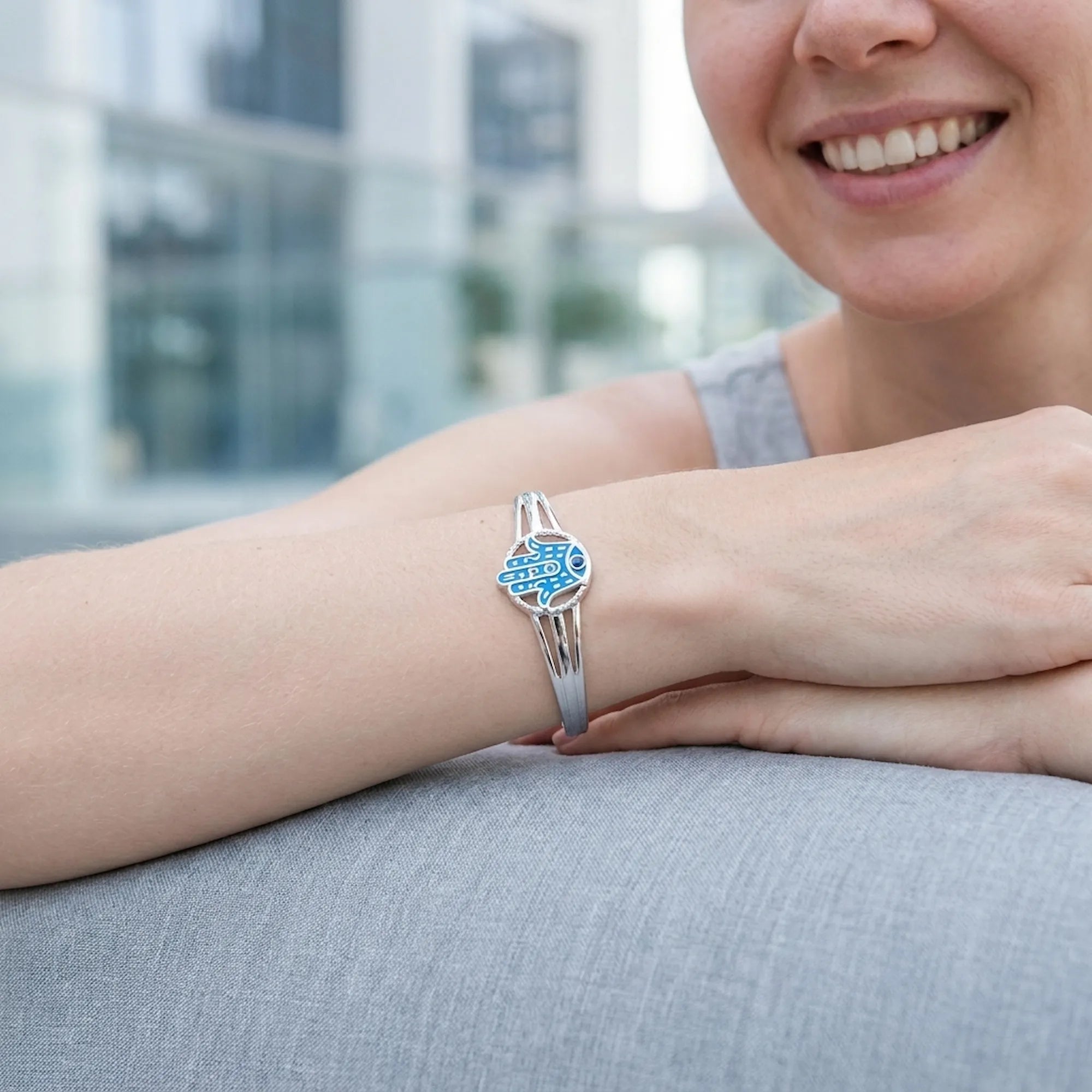 Woman wearing silver Hamsa cuff bangle with azure blue enamel, Dubai urban buildings in background