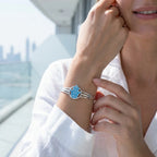 Woman wearing silver Hamsa cuff with powder blue enamel, Dubai skyline waterfront in background
