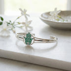 Teal Hamsa silver bangle on marble surface beside white jasmine flowers, opal detail visible in enamel