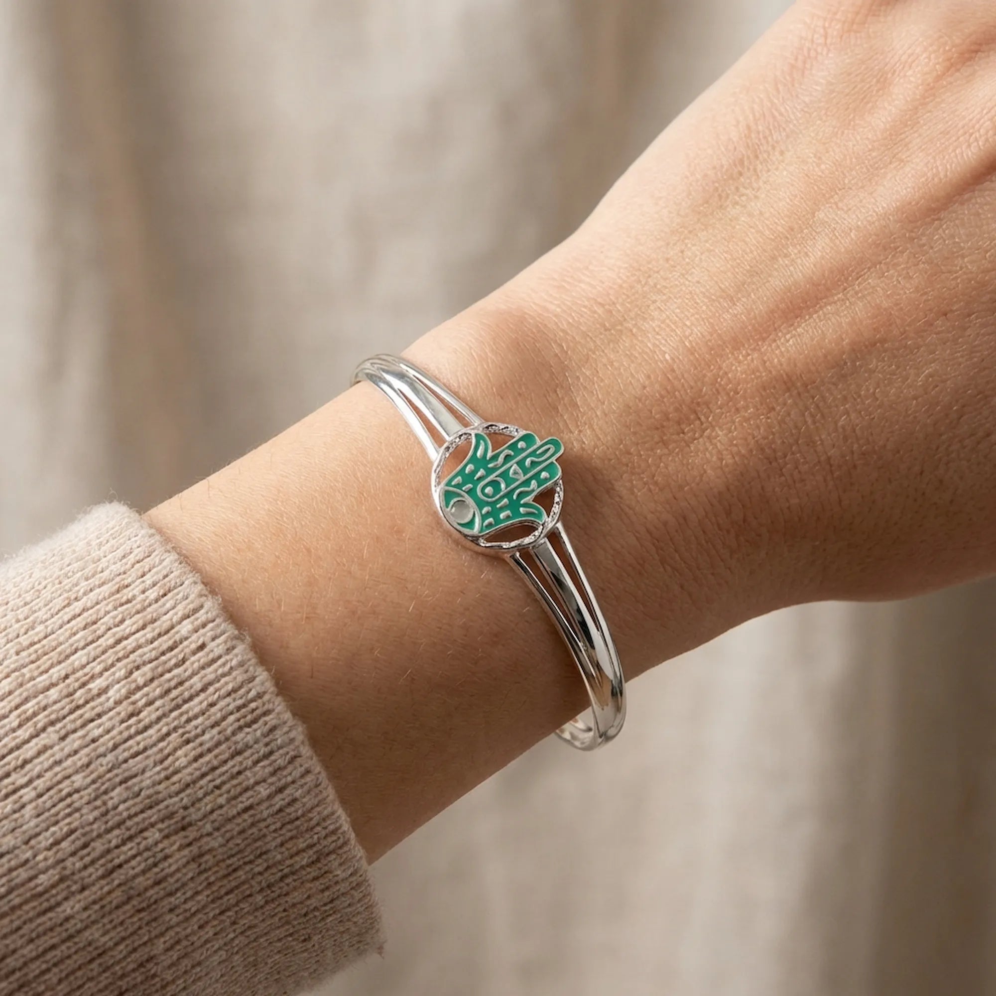 Close-up of teal enamel Hamsa hand with opal stone centre on wrist, fine silver twin bypass band detail