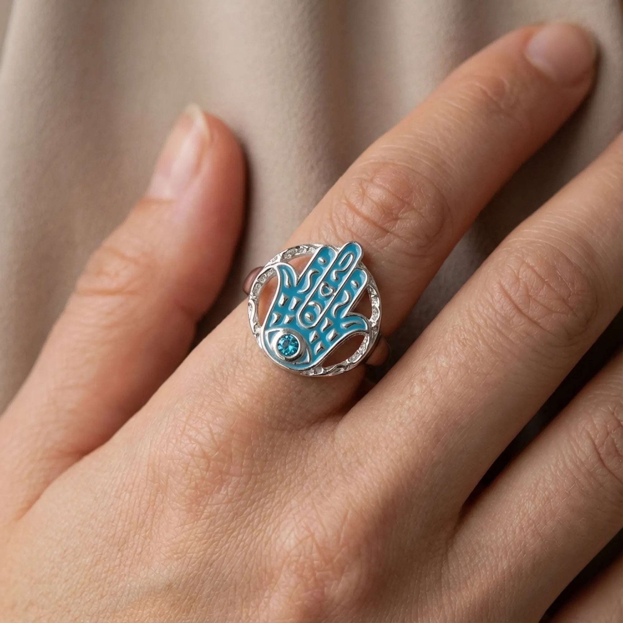 Powder blue enamel hamsa ring in sterling silver worn on the hand, blue topaz eye visible.
