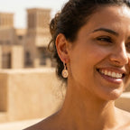 Model wearing Hamsa rose gold pavé drop earrings near Dubai heritage wind towers — Hand of Fatima silver earrings UAE