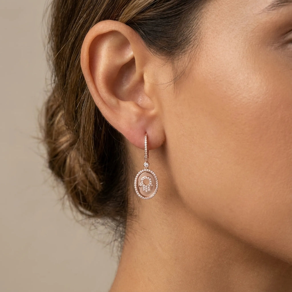 Close-up of rose gold Hamsa oval drop earring on ear — pavé CZ halo and huggie lever-back closure detail