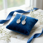 Silver Hamsa drop earrings on blue velvet cushion with white flowers and ribbon — wedding and occasion styling UAE