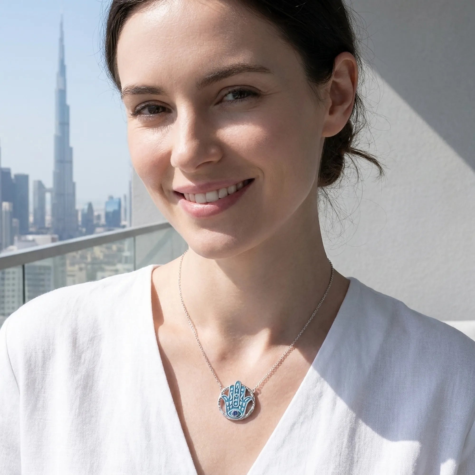 Woman wearing a Hamsa tanzanite pendant necklace with the Burj Khalifa and Dubai skyline behind, Luna Dura.