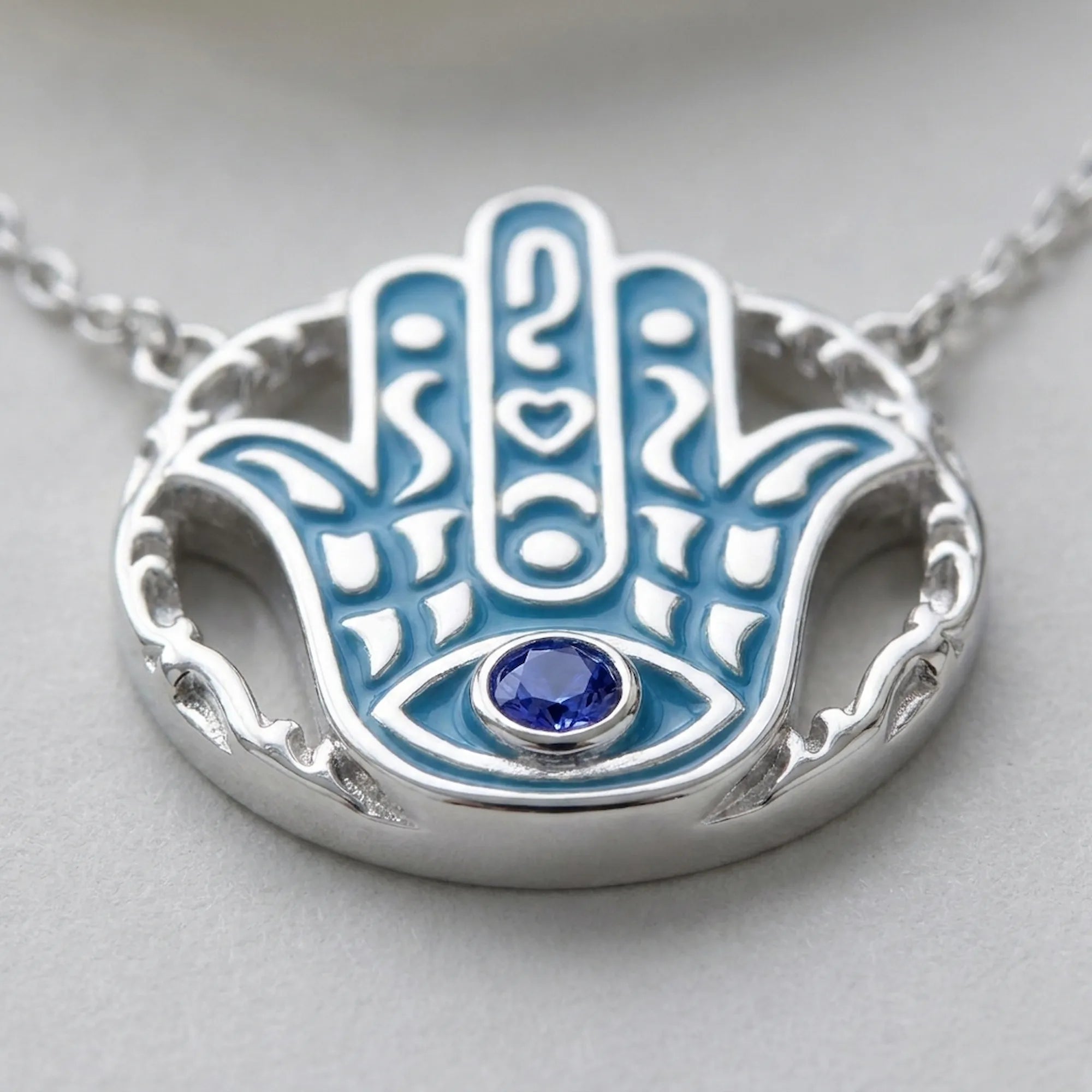 Close-up of a natural tanzanite bezel-set in an azure blue enamel Hamsa pendant, 925 silver, Luna Dura Dubai.