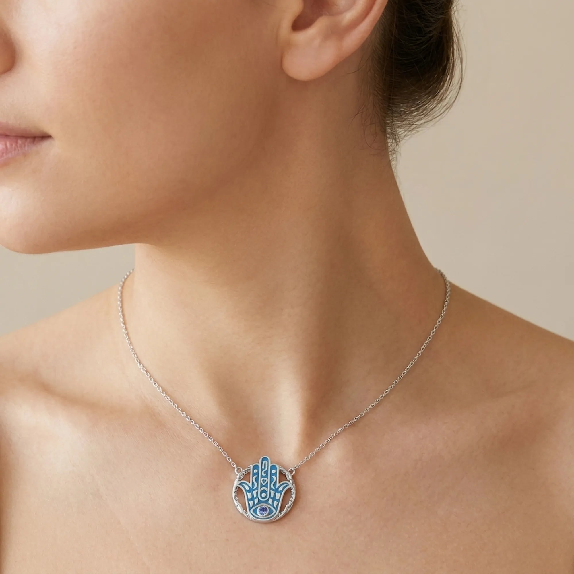 Woman wearing an azure blue Hamsa pendant necklace with a tanzanite eye in 925 silver, Luna Dura Dubai.